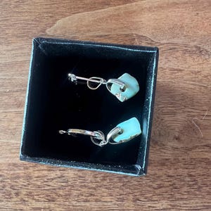 Peut inclure: Une paire de boucles d'oreilles avec un design en m&eacute;tal argent&eacute; et une pierre bleu clair de forme irr&eacute;guli&egrave;re. Les boucles d'oreilles sont pr&eacute;sent&eacute;es dans un coffret noir avec un int&eacute;rieur en velours.
