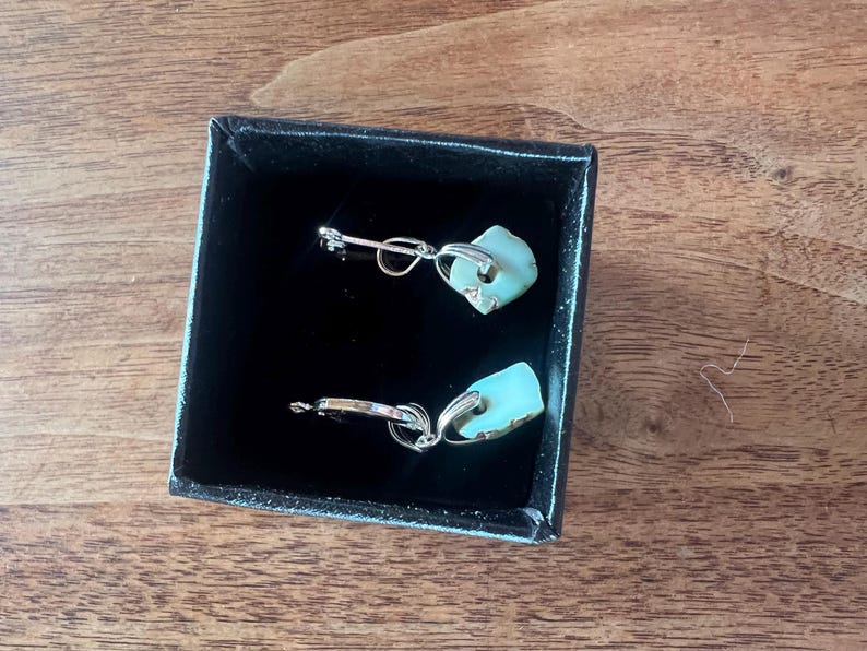 Peut inclure: Une paire de boucles d'oreilles avec un design en m&eacute;tal argent&eacute; et une pierre bleu clair de forme irr&eacute;guli&egrave;re. Les boucles d'oreilles sont pr&eacute;sent&eacute;es dans un coffret noir avec un int&eacute;rieur en velours.