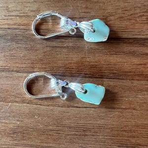 Peut inclure: Une paire de boucles d'oreilles &agrave; crochet argent&eacute;es avec des pendentifs en pierre turquoise de forme irr&eacute;guli&egrave;re. Les boucles d'oreilles sont pr&eacute;sent&eacute;es sur une surface en bois, mettant en valeur leur design et leur couleur.
