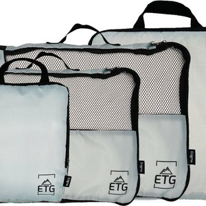 May include: Set of four gray travel packing cubes with black zippers and handles. Each cube has a mesh panel and the logo "ETG" printed on the front.