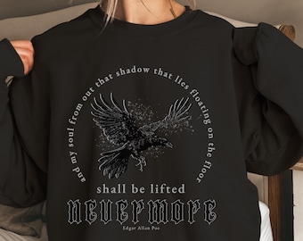 Könnte beinhalten: Schwarzer Pullover mit einem grafischen Aufdruck eines Rabens im Flug mit dem Text "and my soul from out that shadow that lies floating on the floor shall be lifted Nevermore Edgar Allan Poe"