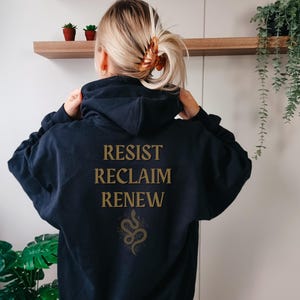 May include: Black hooded sweatshirt with the words "RESIST RECLAIM RENEW" and a gold snake design on the back.