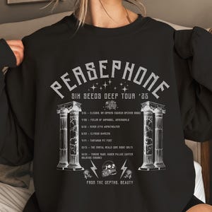 Puede incluir: Sudadera negra con un diseño gráfico blanco con el texto "PERSEPHONE SIX SEEDS DEEP TOUR '25" y un calendario de la gira. El gráfico también incluye dos columnas, una calavera y rayos.