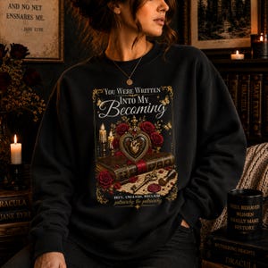 Puede incluir: Sudadera negra con un diseño que incluye el texto "You Were Written Into My Becoming", un medallón en forma de corazón, rosas y velas. El diseño también incluye el texto "Defy, Unleash, Reclaim patriarchy the patriarchy."