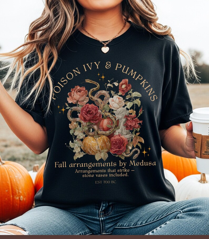 May include: Black t-shirt with a floral and snake design. The design includes pumpkins, roses, and the text "POISON IVY & PUMPKINS". Below the design is the text "Fall arrangements by Medusa" and "EST 700 BC".