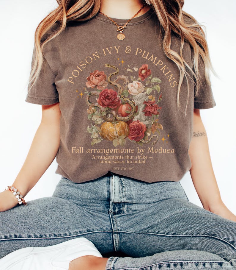 May include: Brown t-shirt with the text "POISON IVY & PUMPKINS" in an arch. Below the text is a floral arrangement with roses, pumpkins, and a snake. The text "Fall arrangements by Medusa" is below the floral arrangement.