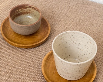 May include: Two ceramic bowls with speckled glaze, one brown and one white, on wooden coasters. The bowls are empty and ready to be used.