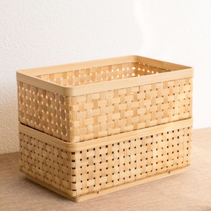 Pode incluir: Duas cestas de armazenamento de bambu natural trançado empilhadas uma em cima da outra. As cestas são retangulares e têm um padrão trançado.
