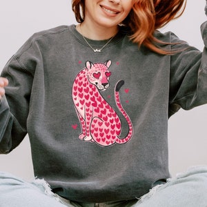 May include: A gray sweatshirt with a pink leopard print design. The leopard has hearts for spots and heart-shaped eyes.