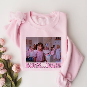 May include: A light pink crewneck sweatshirt featuring a rectangular graphic print of several children in a bedroom setting. The text "BOYS...UGH!" is printed in pink letters with a black outline below the image of the children.
