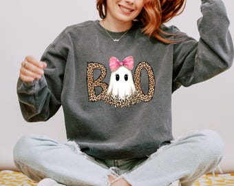 May include: A charcoal gray crewneck sweatshirt featuring a graphic print of a white ghost with a pink bow and leopard print accents. The letters B and O are also in a leopard print pattern, completing the word BOO on the front of the garment.