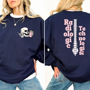 May include: Navy blue sweatshirt with a pink skull and coffee cup graphic on the front and the text "Radiologic Technologist" with a pink spine graphic on the back.