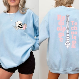 May include: Light blue sweatshirt with a skeleton drinking coffee on the front and the text "Radiologic Technologist" with a spine graphic on the back.
