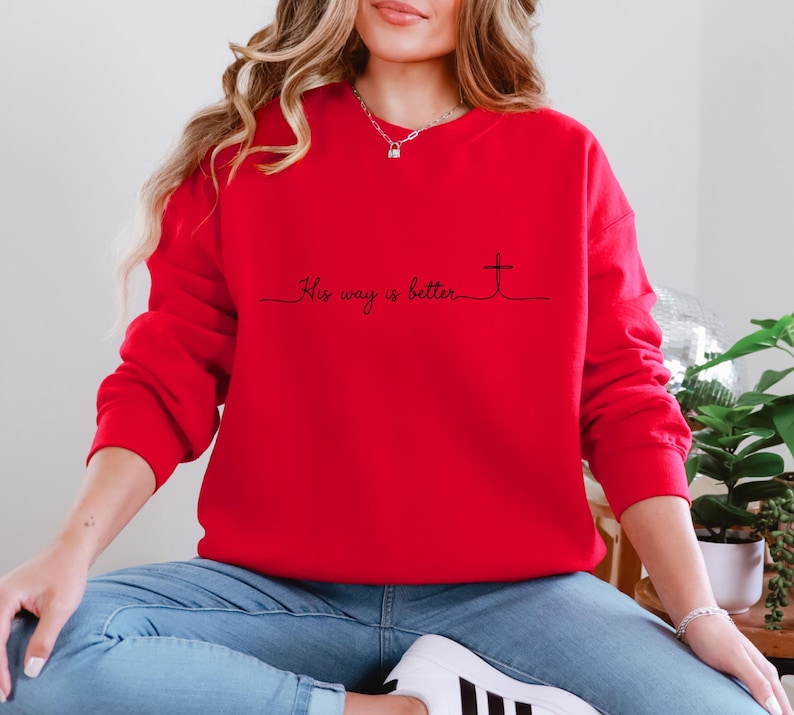 May include: A bright red sweatshirt with the phrase "His way is better" and a cross design in black. The long-sleeved top is made of a soft material and is suitable for casual wear.