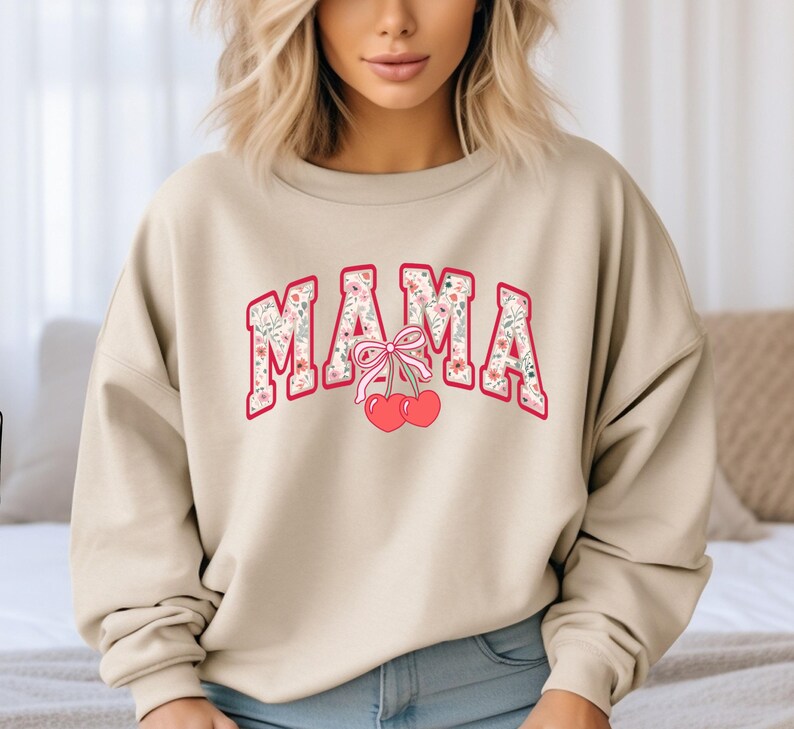 Może przedstawiać: Beżowa bluza z nadrukiem kwiatowym i napisem "MAMA" w kolorze czerwonym z r&oacute;żową kokardką i wiśniami.