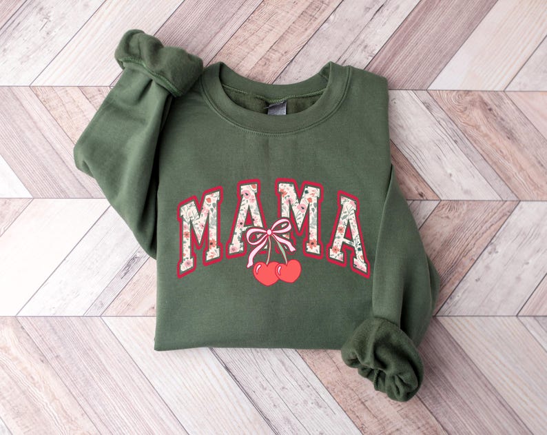 Może przedstawiać: Zielona bluza z napisem "MAMA" w kwiatowym wzorze i dwiema czerwonymi wiśniami z r&oacute;żową kokardką.