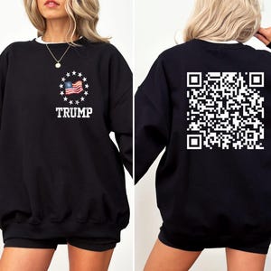 May include: Black sweatshirt with a white American flag and the word "TRUMP" printed on the front. The back of the sweatshirt has a white QR code printed on it.