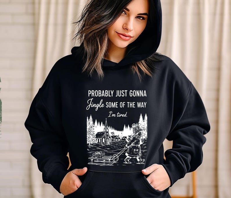 Puede incluir: Sudadera con capucha negra con el texto "Probably just gonna jingle some of the way, I'm tired." Un gr&aacute;fico en blanco y negro representa a una persona tirando de un trineo con regalos hacia una iglesia en una escena invernal.