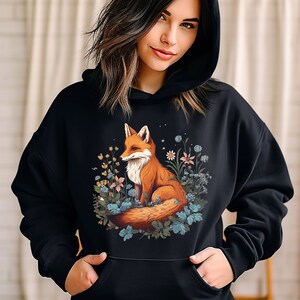 May include: A black hooded sweatshirt featuring a graphic print of a red fox sitting among various blue and yellow flowers and green leaves. The hoodie includes a front kangaroo pocket and long sleeves, providing a casual and comfortable garment.