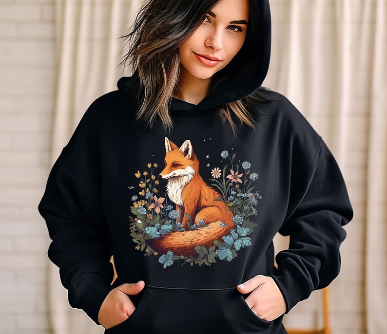 May include: A black hooded sweatshirt featuring a graphic print of a red fox sitting among various blue and yellow flowers and green leaves. The hoodie includes a front kangaroo pocket and long sleeves, providing a casual and comfortable garment.