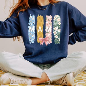 Pu&ograve; includere: Una felpa blu navy con un design floreale e la parola "MAMA" stampata sul davanti.