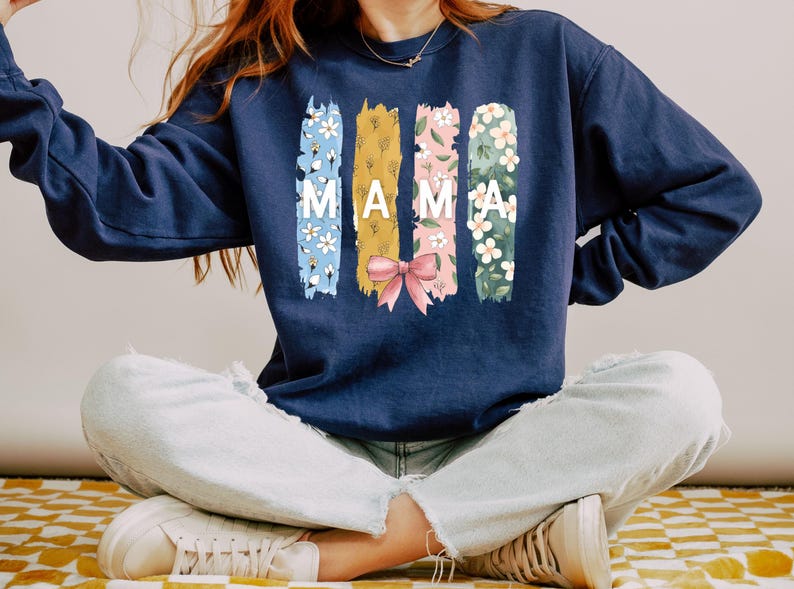 Pu&ograve; includere: Una felpa blu navy con un design floreale e la parola "MAMA" stampata sul davanti.