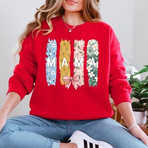 Pu&ograve; includere: Felpa rossa con un design floreale e la parola "MAMA" stampata sul davanti.