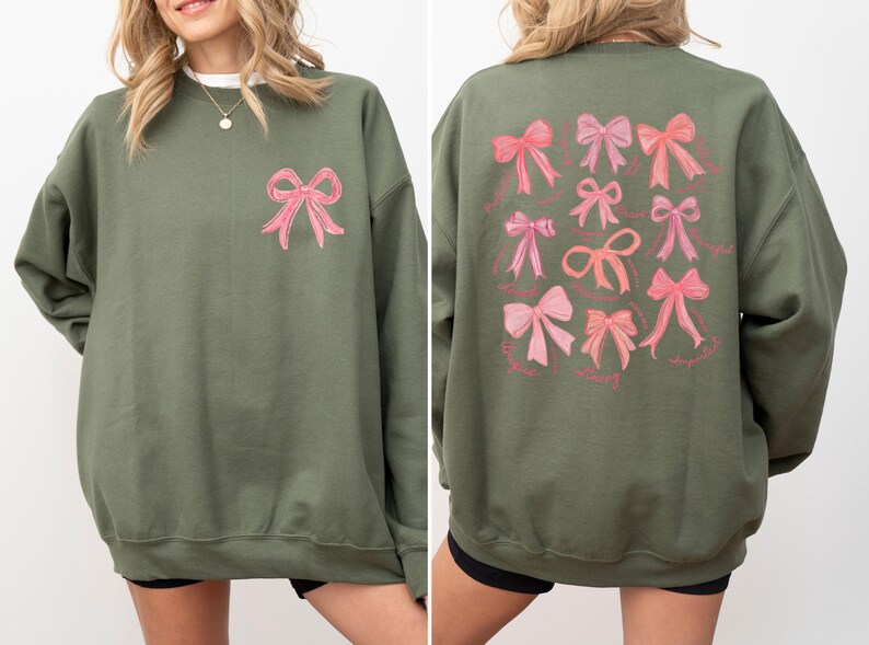 May include: An olive green crewneck sweatshirt featuring a single pink bow graphic on the upper left chest and a large collection of various pink bow illustrations printed on the back, each accompanied by small cursive text labels below the bows.