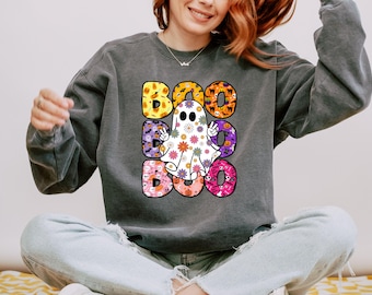 May include: A charcoal gray crewneck sweatshirt featuring a large graphic print of the word BOO repeated three times. The letters are filled with Halloween patterns, and a white ghost with a colorful floral print makes a peace sign in the center.