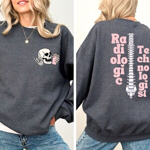 May include: A dark gray sweatshirt with a pink skeleton holding a coffee cup on the front and the words "Radiologic Technologist" spelled vertically down the spine on the back.