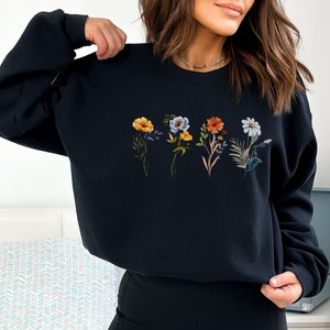 May include: Black sweatshirt with a floral print featuring five different flowers in shades of yellow, orange, blue, and white.