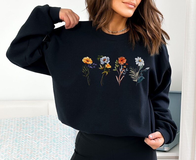 May include: Black sweatshirt with a floral print featuring five different flowers in shades of yellow, orange, blue, and white.