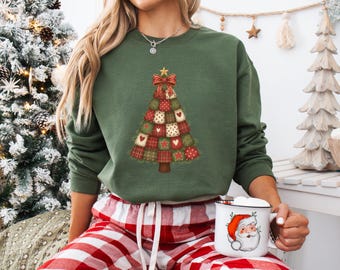 Può includere: Felpa verde con un design ad albero di Natale composto da quadrati patchwork, cuori e stelle. L'albero è sormontato da un fiocco rosso e una stella dorata. La persona indossa pantaloni del pigiama a quadri rossi e bianchi e tiene in mano una tazza di Babbo Natale.