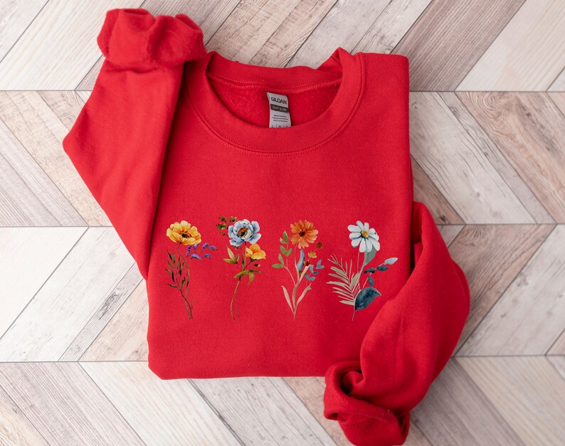 May include: Red sweatshirt with a floral design featuring yellow, orange, white, and blue flowers.