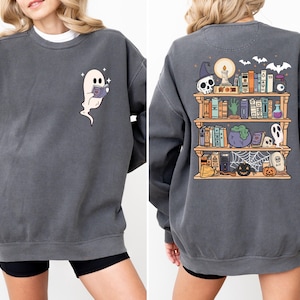 Op de afbeelding: Donkergrijze sweatshirt met een lezende geest op de voorkant en een Halloween-thema boekenplank op de achterkant. Het ontwerp op de rug bevat een schedel, vleermuizen, boeken en een ketel. Een comfortabele, casual stijl.