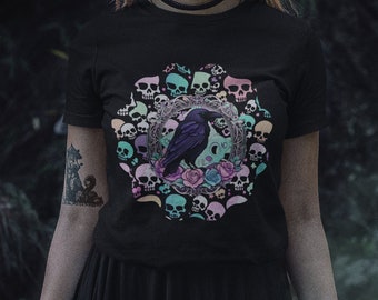 Könnte beinhalten: Ein schwarzes T-Shirt mit einem bunten Motiv eines Rabens, der auf einem zunehmenden Mond sitzt, umgeben von Schädeln und Blumen.