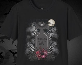 Op de afbeelding: Zwart t-shirt met een gotisch ontwerp met een grafsteen, bomen en een volle maan. De grafsteen leest "HERE LIES MY LAST FUCK" met bloemen aan de basis. Het ontwerp heeft een griezelig Halloween-thema.
