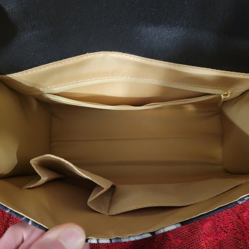 Pode incluir: O interior de uma bolsa com padr&atilde;o preto e branco com forro bege. A bolsa tem um bolso com z&iacute;per e um bolso aberto menor.