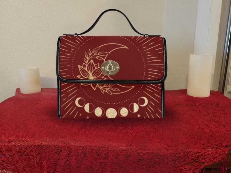 Pode incluir: Uma bolsa de m&atilde;o vermelha com al&ccedil;a preta e um design dourado de lua e flores. A bolsa tem um fecho prateado e um design dourado de fases lunares.