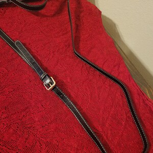 Pode incluir: Uma tira de couro preta com uma fivela prateada sobre um fundo de tecido vermelho.