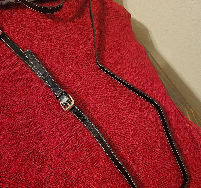 Pode incluir: Uma tira de couro preta com uma fivela prateada sobre um fundo de tecido vermelho.
