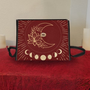Pode incluir: Uma bolsa tote vermelha com um design de lua dourada e flores. A bolsa tem uma al&ccedil;a preta e um design de fases lunares douradas.