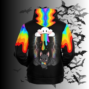 May include: A black hoodie featuring a rainbow-colored hood and sleeve accents. The back displays a graphic of a white cloud with a rainbow drip, lightning bolts, and a small gray bat wearing a rainbow bowtie, all set against a black background.