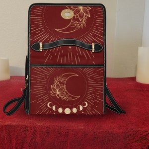 Pode incluir: Uma mochila de couro vermelha com um design de lua dourada e flores. A mochila tem uma al&ccedil;a preta e uma fivela dourada.