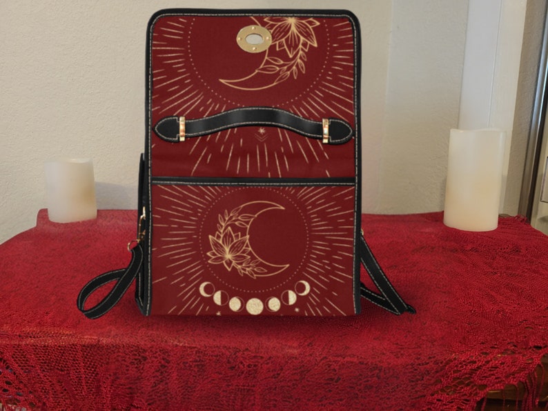 Pode incluir: Uma mochila de couro vermelha com um design de lua dourada e flores. A mochila tem uma al&ccedil;a preta e uma fivela dourada.