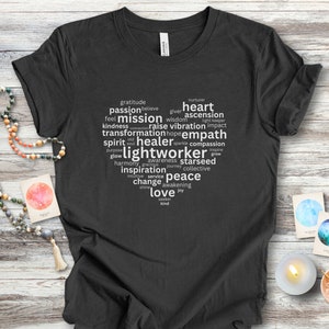 May include: A dark gray t-shirt with a white word cloud design. The words include "gratitude", "passion", "mission", "heart", "ascension", "lightworker", "empath", "peace", and "love".