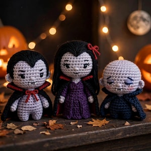 May include: Three crocheted dolls featuring vampire-inspired designs. The left doll has black hair and a black cape with a red lining. The center doll has long black hair with a red bow and a purple dress. The right doll is bald with a dark blue cape.