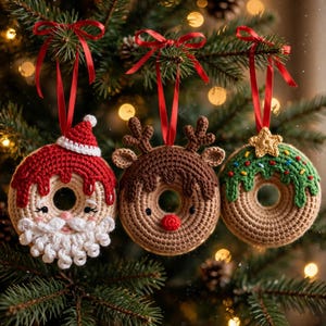 May include: Three crocheted doughnut ornaments hanging from red ribbons. The first is a Santa doughnut with a red hat and white beard. The second is a brown reindeer doughnut with antlers and a red nose. The third is a green frosted doughnut with a star.