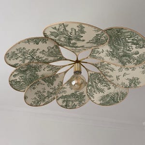 Op de afbeelding: Een plafondlamp met een bloemenpatroon op de lampenkappen. De lampenkappen zijn gevormd als bloemblaadjes en zijn in een cirkelvormig patroon gerangschikt. De lamp is gemaakt van metaal en heeft een gouden afwerking.