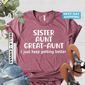 May include: A maroon t-shirt with white text that reads "Sister Aunt Great-Aunt I just keep getting better".